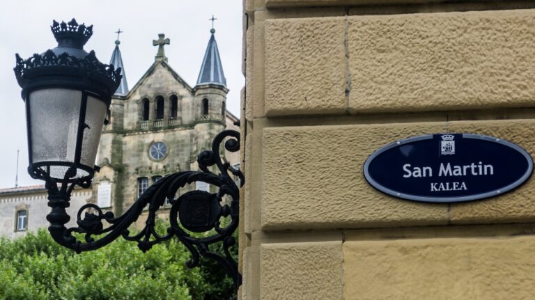 Gadeskilt for San Martin kalea i San Sebastián med en gammel gadelygte og Buen Pastor-katedralen i baggrunden